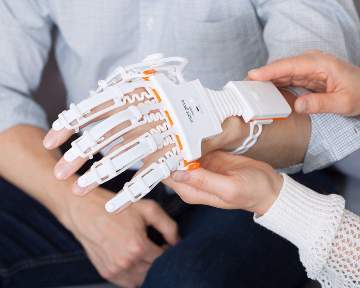 Ergotherapeutin legt einem Patienten den sensorbasierten NEOFECT Smart Glove zum Hand-Rehabilitationstraining an